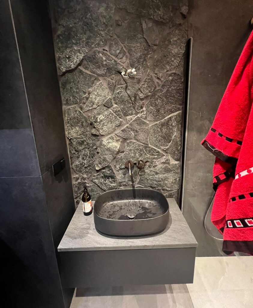 łazienka w ciemnej tonacji, widok na umywalkę i ścianę wyłożoną ciemnymi kawałkami skały, apartament w Gdyni