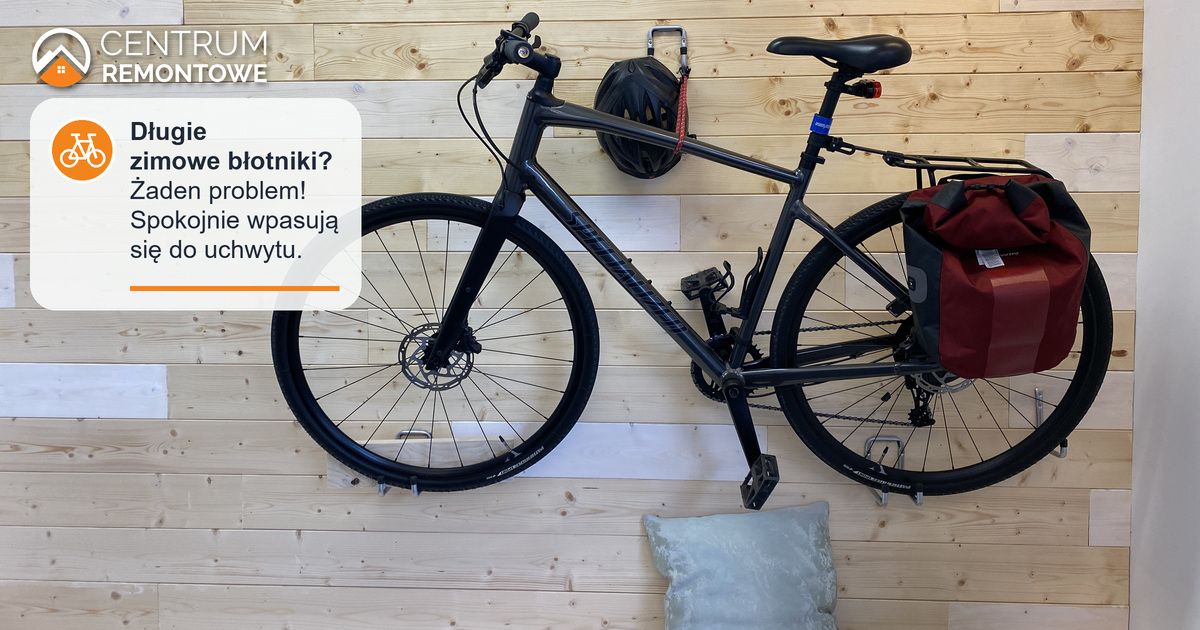 Rower z błotnikami i sakwą umieszczony na uchwycie, który jest zamocowany na drewnianej ścianie, kask powieszony na haku (także umieszczony na ścianie)