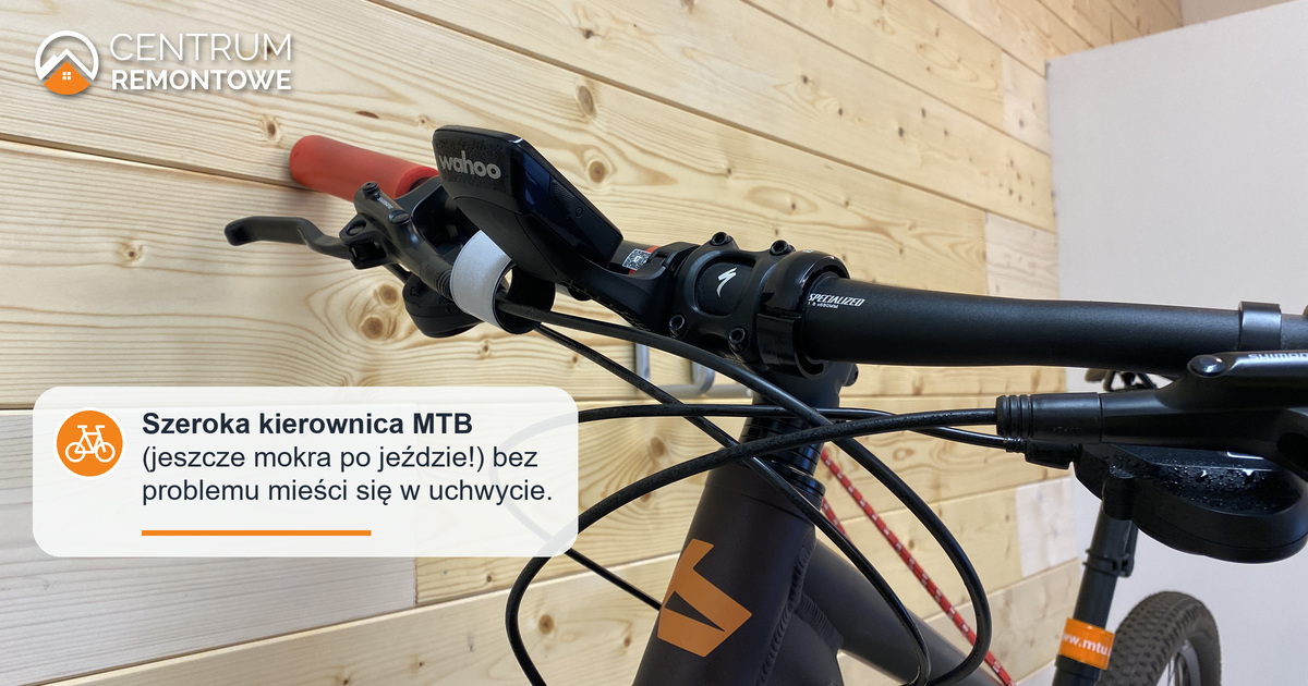 Szeroka kierownica roweru górskiego mieści się spokojnie na uchwycie rowerowym zamontowanym na ozdobnej drewnianej ściance w domu