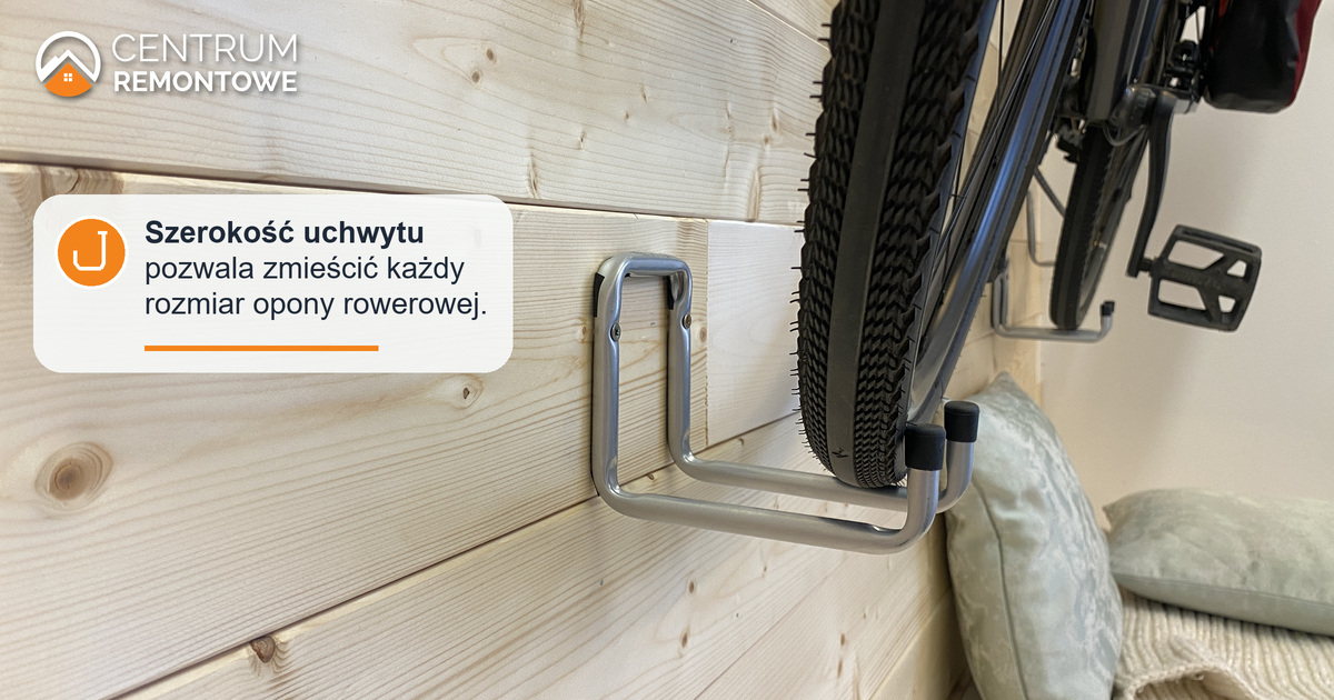 Opona roweru spoczywa w podwójnym metalowym haku przykręconym do drewnianej ściany. Model opony to Specialized Pathfinder Sport 38 mm, doskonale mieści się w tym uchwycie rowerowym.