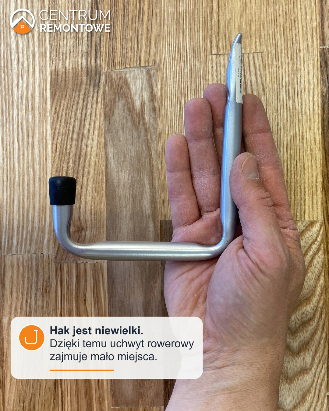 Porównanie wielkości elementu do męskiej dłoni - metalowy hak ścienny z gumową nasadką trzymany w dłoni - jest to element uchwytu na rower.