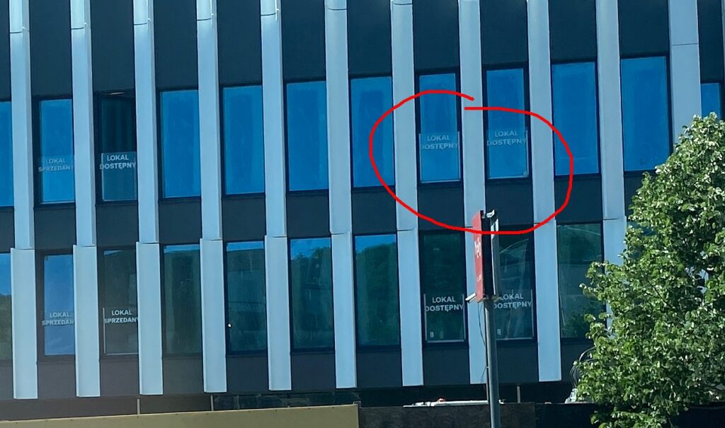 Budynek w stanie deweloperskim - zbliżenie na fasadę z widocznymi napisami dotyczącymi dostępności lokali komercyjnych.